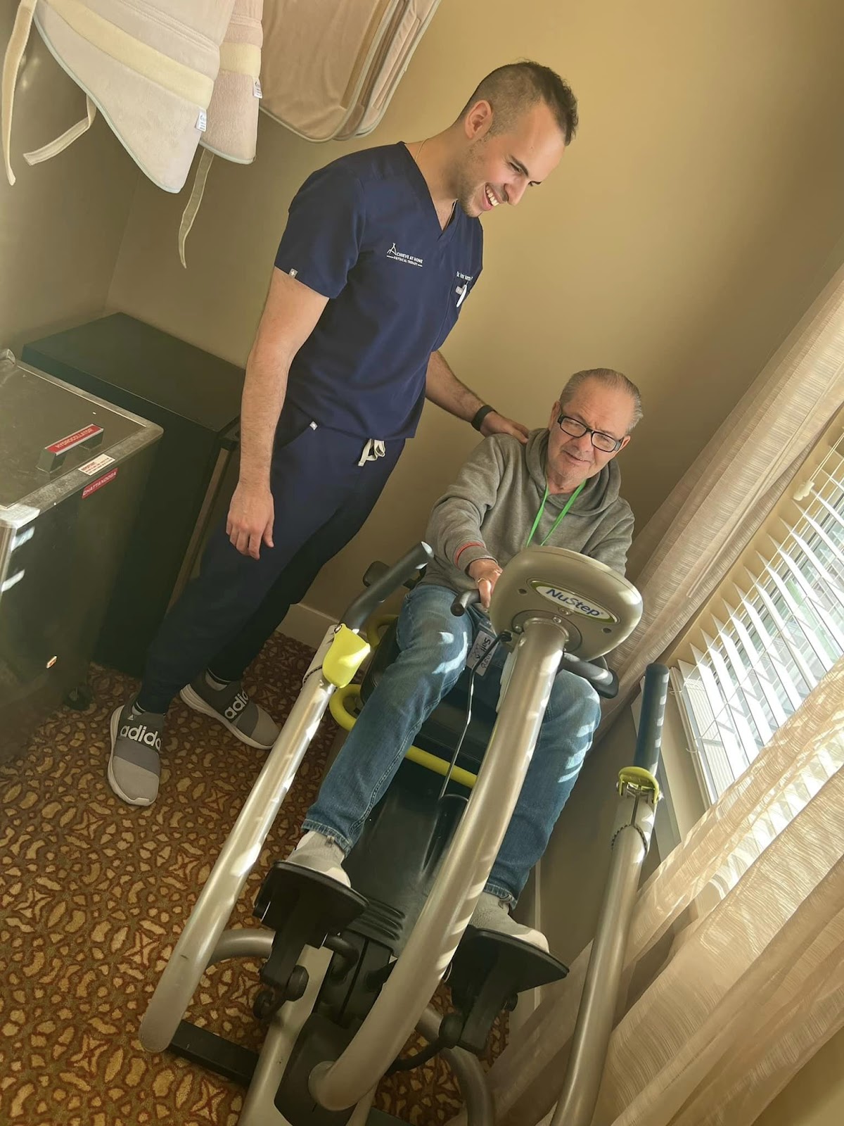 A physical therapist smiling at a resident who is on a seated stationary bicycle