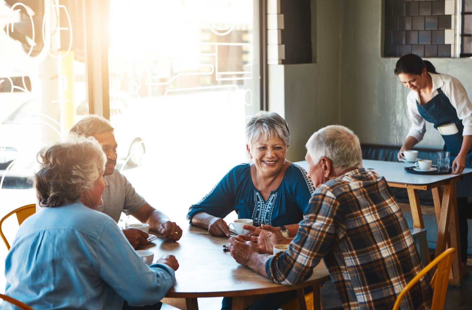 A group of smiling seniors enjoy each other's company as they start their day with a cup of coffee.