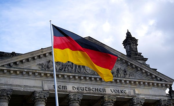 Bundestag building in Berlin, Germany with German flag waving prominently in the foreground - symbolizing Germany's political and economic influence.