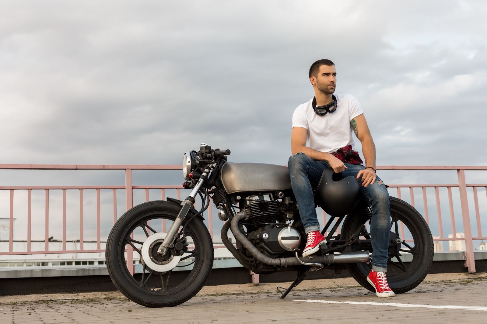 Rider sitting on café racer style motorcycle with helmet in hand