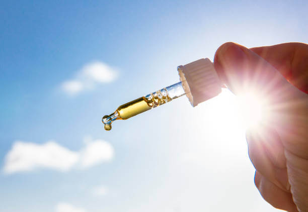 A hand holding a glass dropper filled with golden liquid vitamin D.