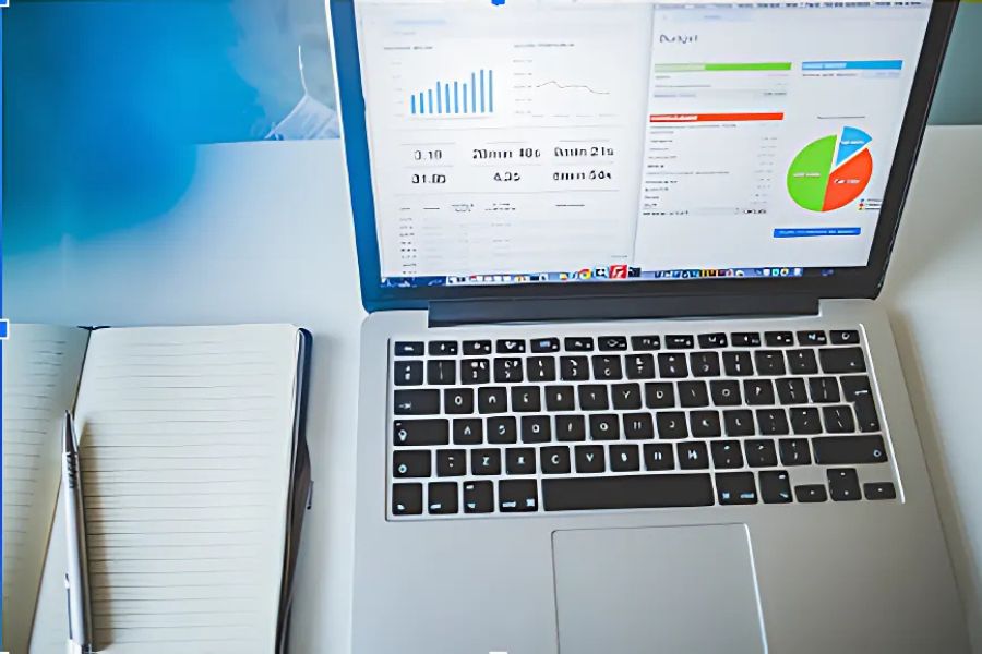 Laptop displaying budget analysis with graphs and notebook beside it