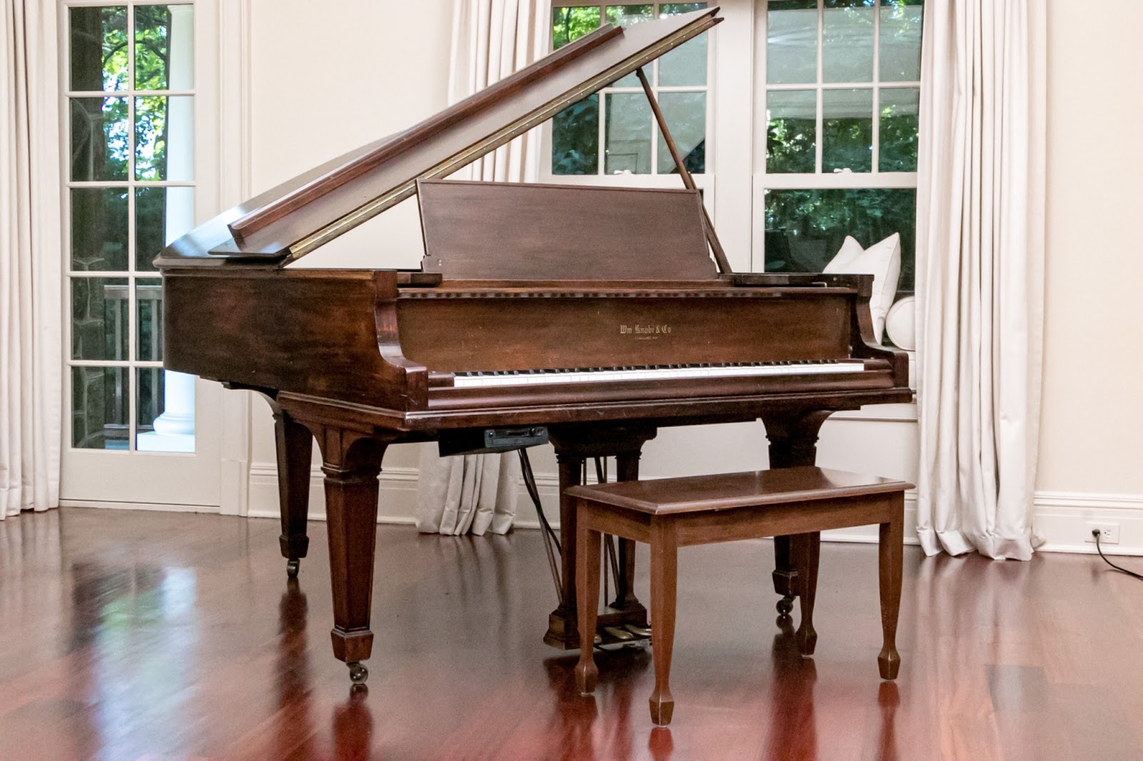 Walnut framed baby grand piano with bench in a white room.