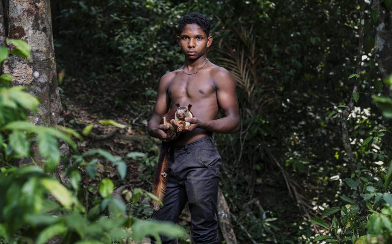 A photo of a young man in the forest holding his pet Malabar giant squirrel. 