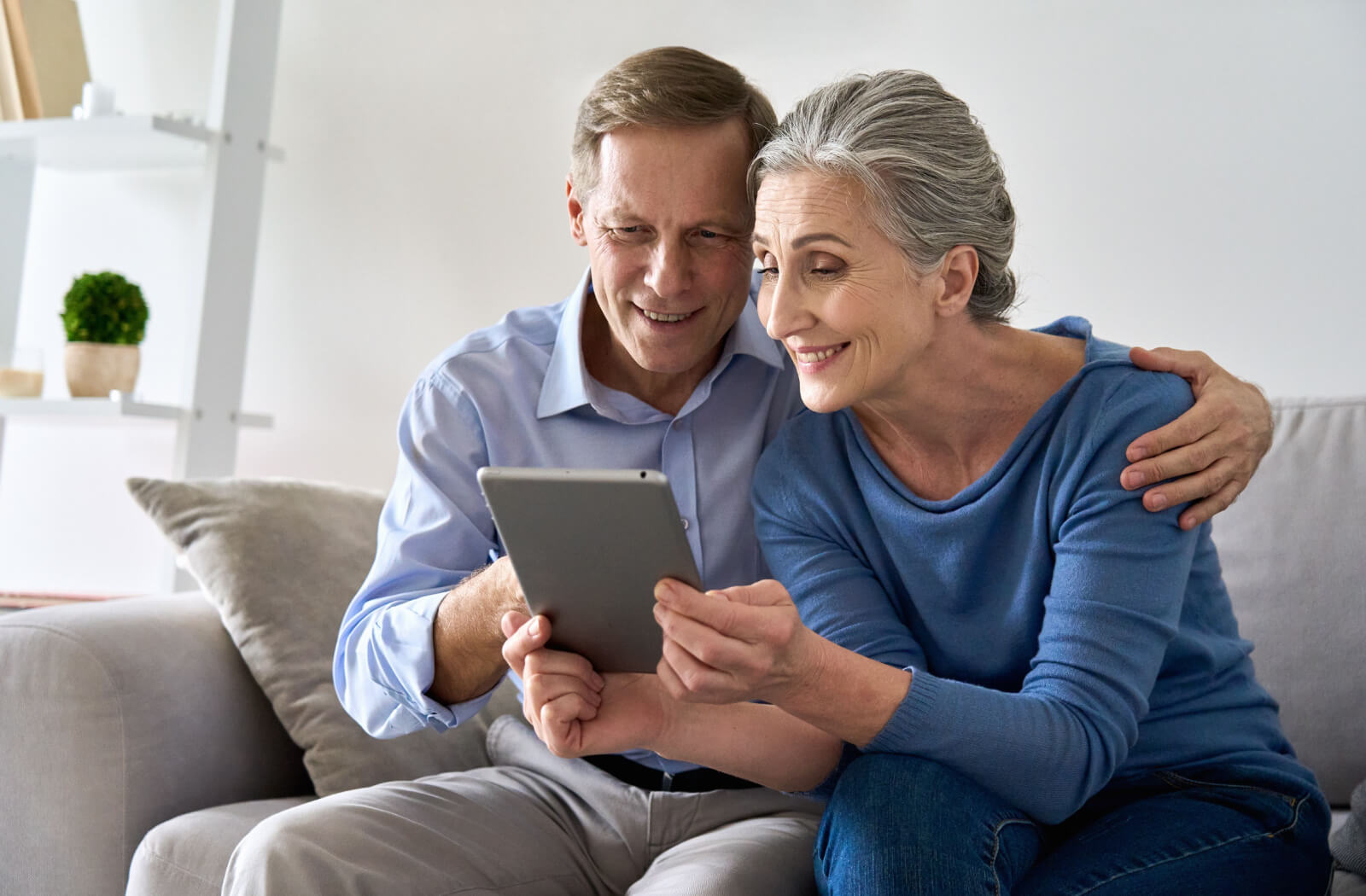 An older couple holding a tablet up during a phone call to stay connected with their family.