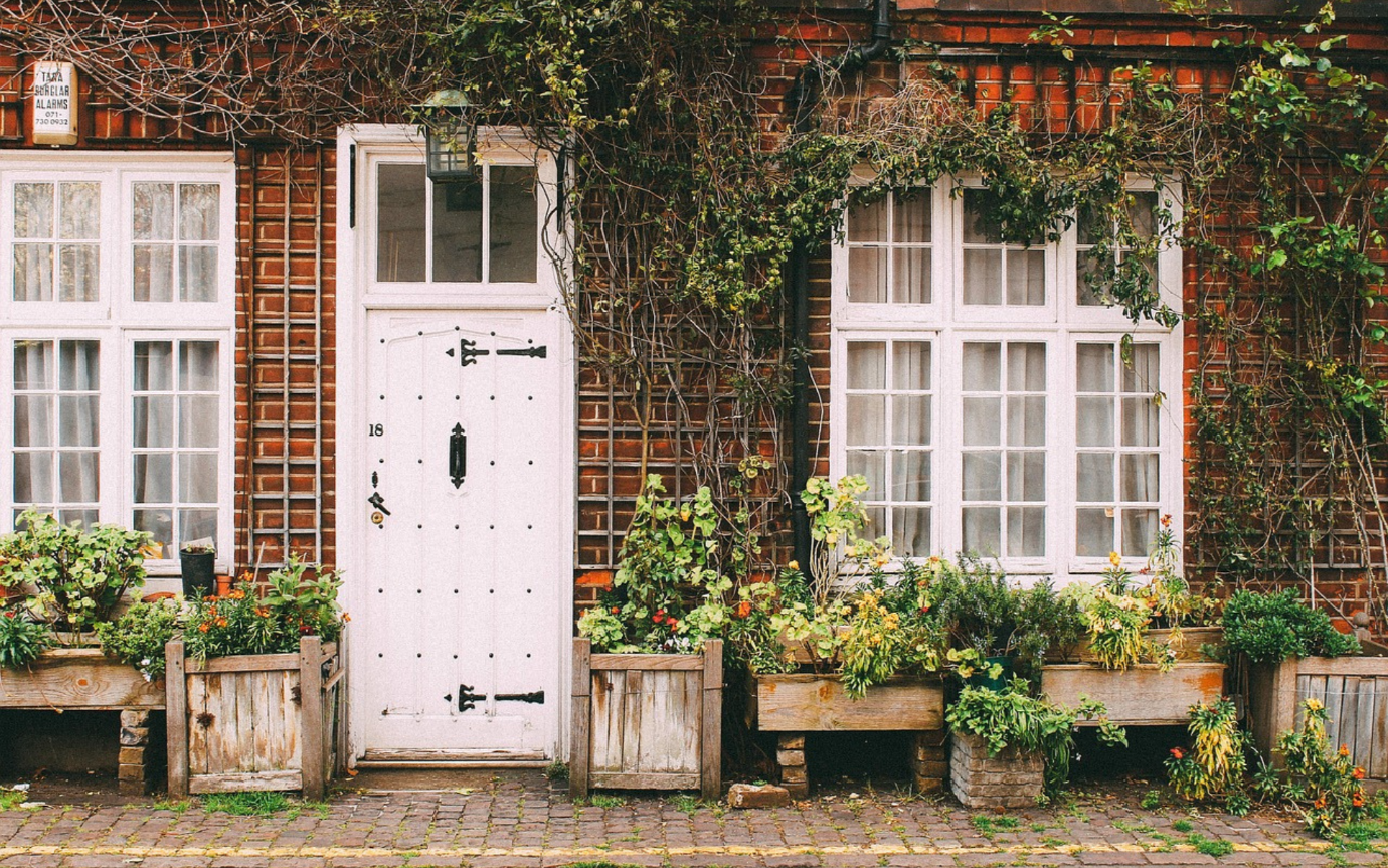 A white door and windows with plants growing on the side of a brick buildingDescription automatically generated