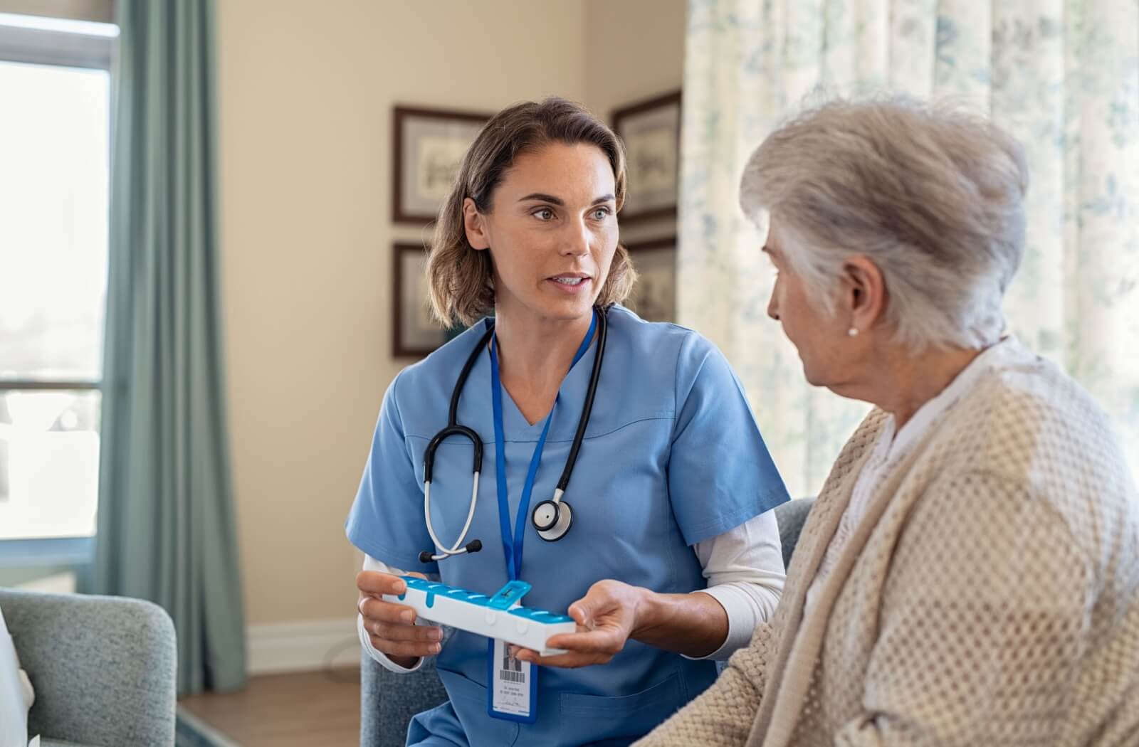 A nurse explains to a senior how to better remember their medication using a week-based pill storage system