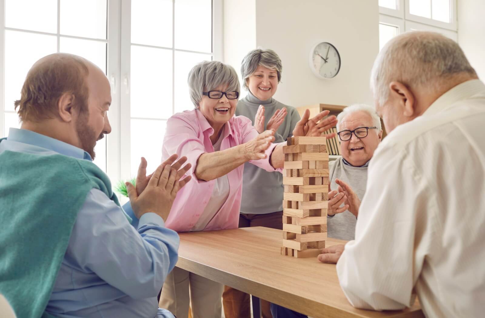 A group of happy seniors playing a block-stacking game together in the common area of their senior living community.