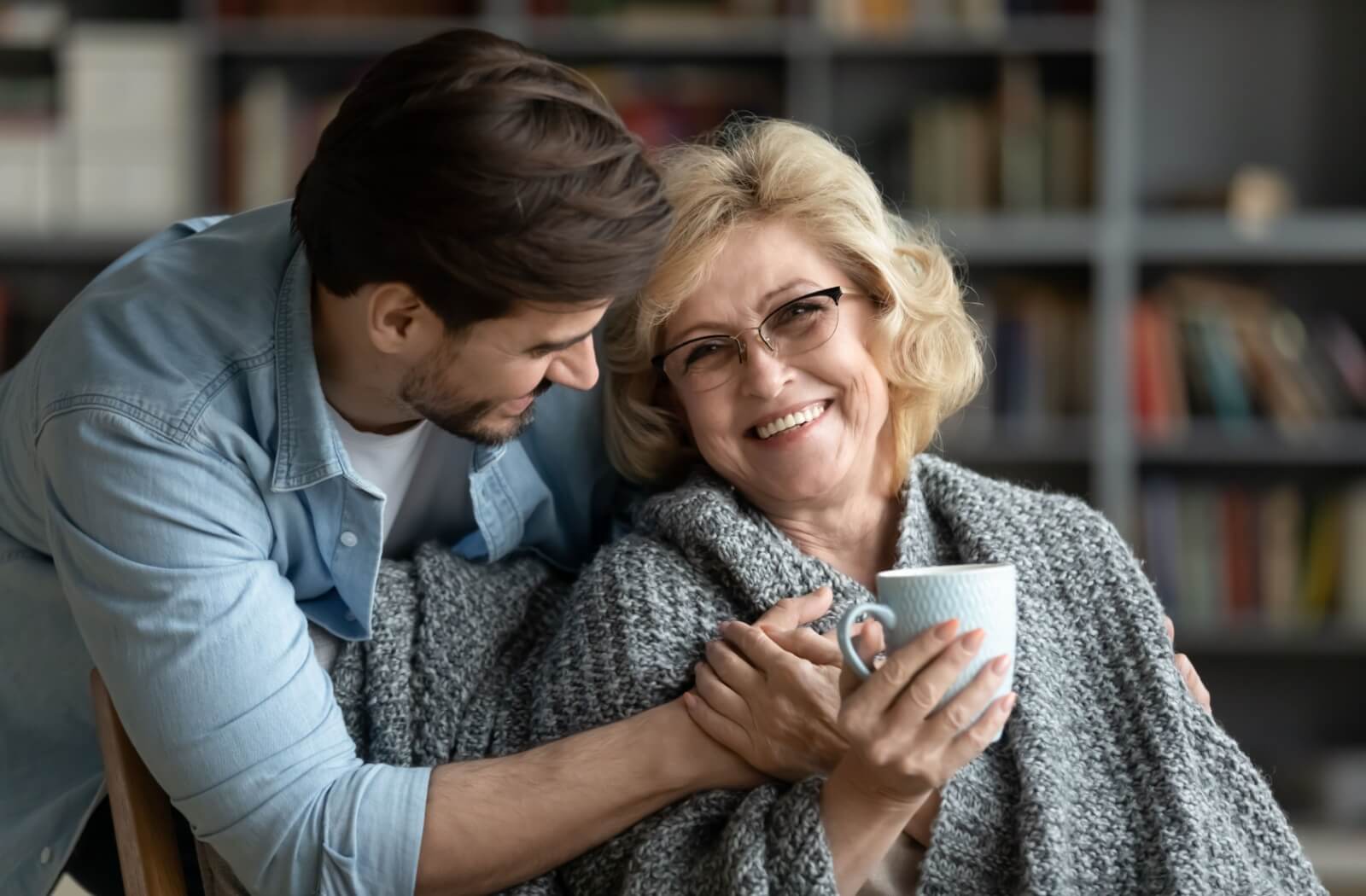 An adult brings their senior parent a tea and checks in on them.