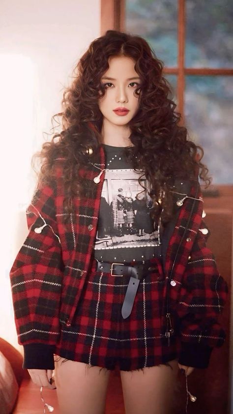 This contain A picture of BLACKPINK's Jisoo with long curly hair wearing a red and black plaid jacket, posing in front of a window