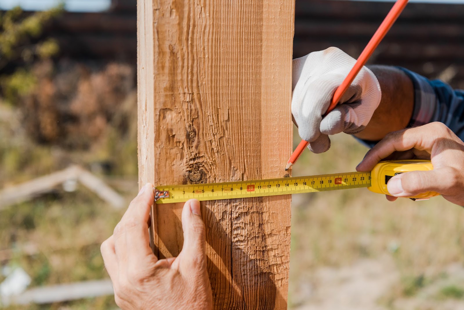 Two people messing a fence using a pencil and a tape measure. 