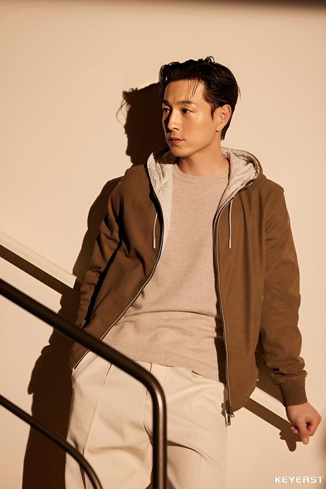 This may contain of Jung Sung Il standing next to a hand rail wearing a brown jacket and khaki pants