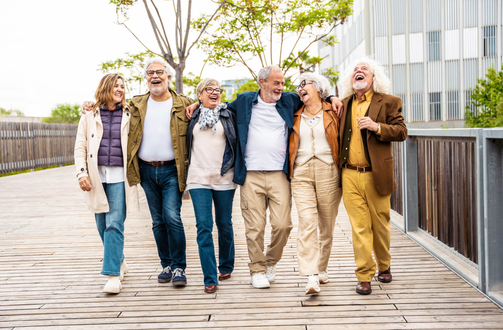 A group of senior friends outdoors laughing with their arms around each other's shoulders.