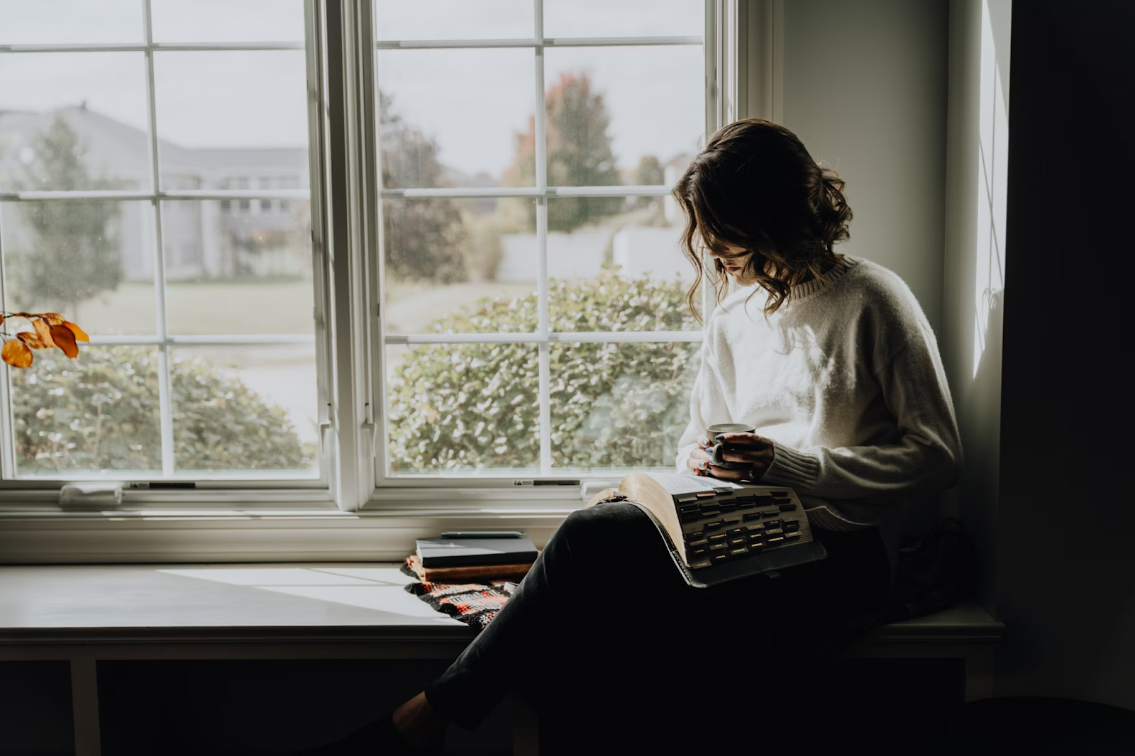 Citing short stories in MLA format. A woman sits on a window sill reading an anthology with a coffee. She is learning how to write a works cited entry for a short story in MLA.
