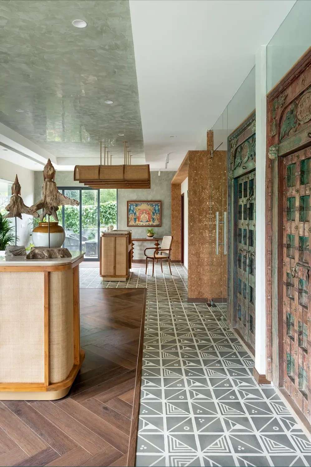 A spacious, modern office interior features a mix of wood and tile flooring. A wooden reception desk sits to the left with decorative sculptures inspired by India.