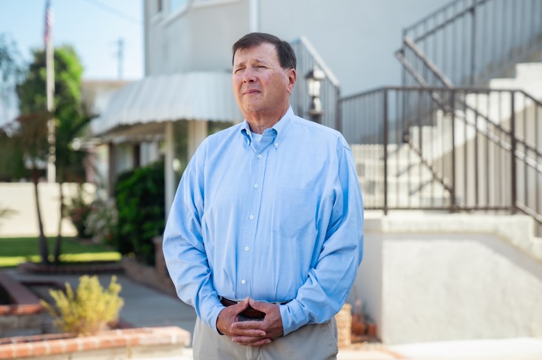 Wearing a light blue button-down shirt and khaki pants, Mike Placido stands in front of a bright white four-unit rental property he and his wife own and manage on August 12, 2024. Photo: Jules Hotz for CalMatters