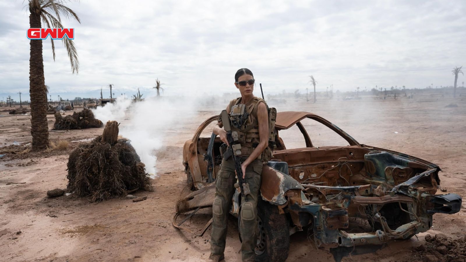 Laysla De Oliveira portraying Cruz, with a rifle stands near a destroyed car in battle.