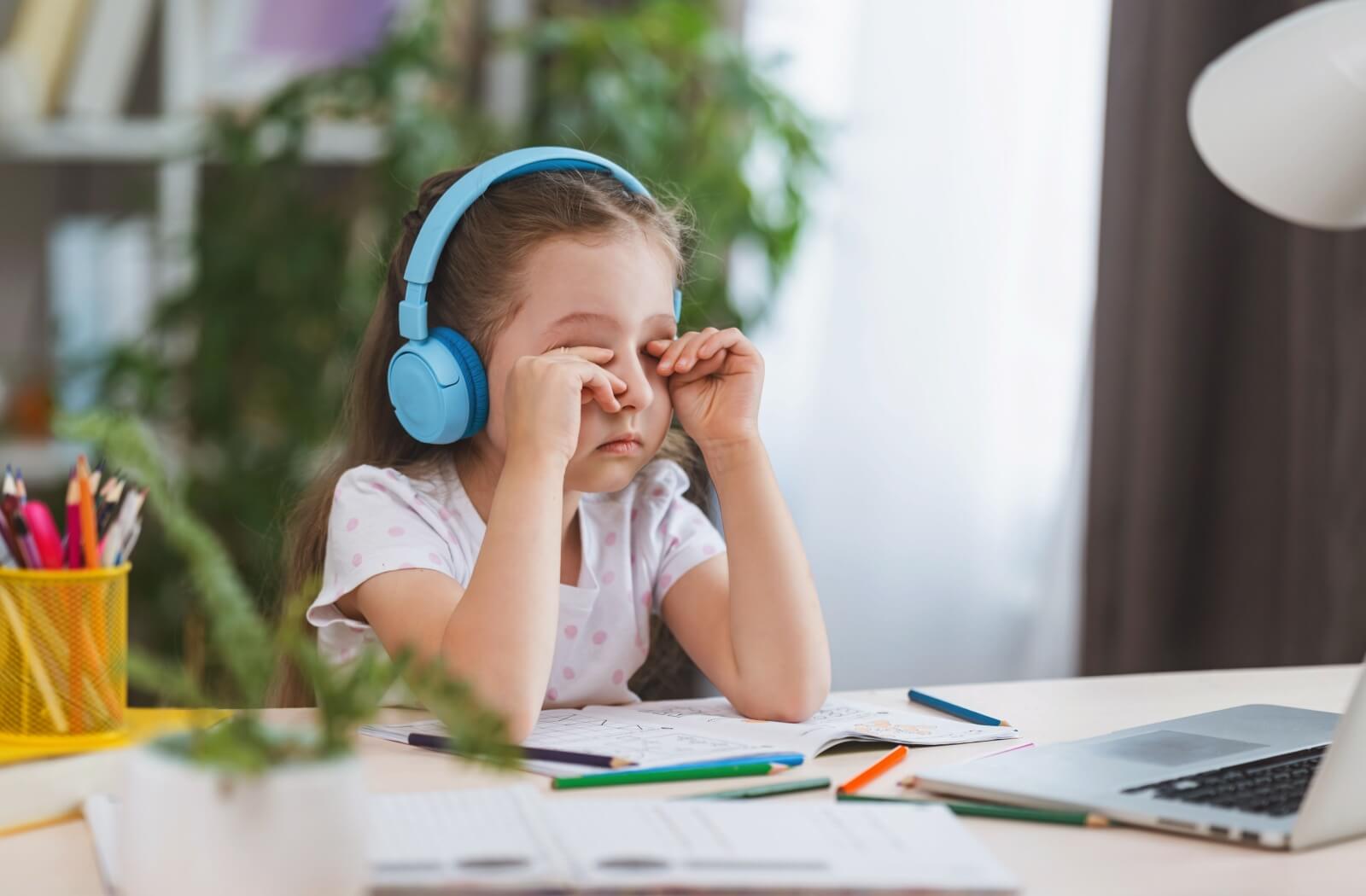 A young child rubbing their eyes because of a headache from vision issues and eye strain.