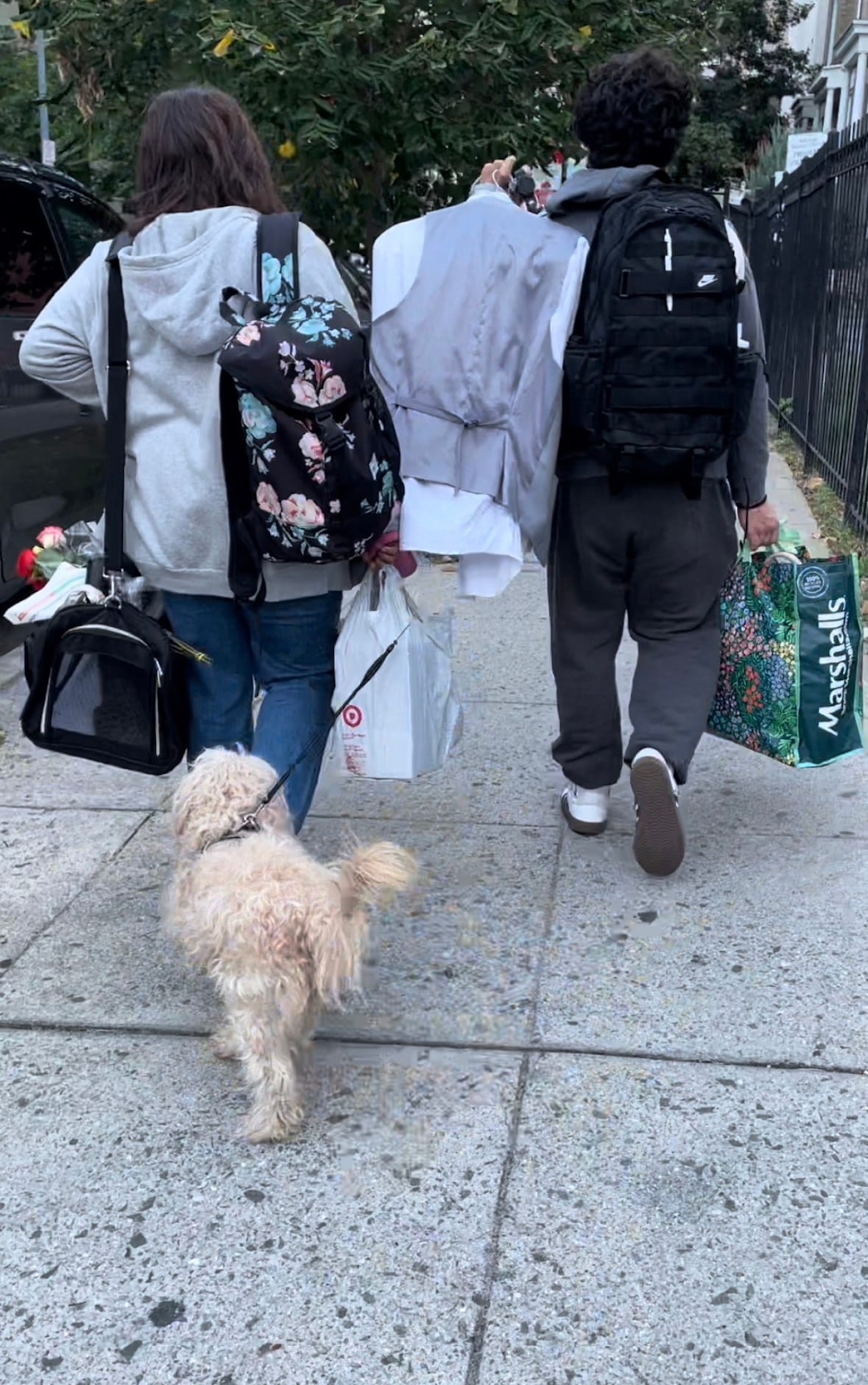 Imagen muestra dos personas caminando d espaldas con maletas, bolsas y un perro. 