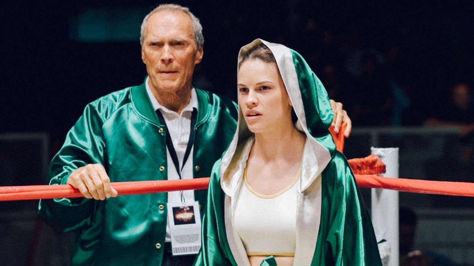 Clint Eastwood junto a Hilary Swank en el ring de boxeo, ambos usando chaquetas verdes en una escena de 'Million Dollar Baby', listos para el combate.