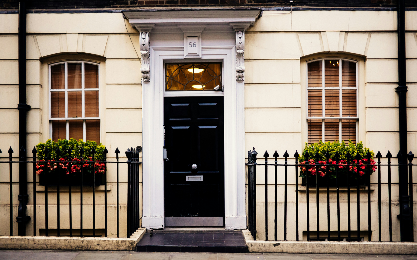 A black door with a black railing and flowers in front of a buildingDescription automatically generated