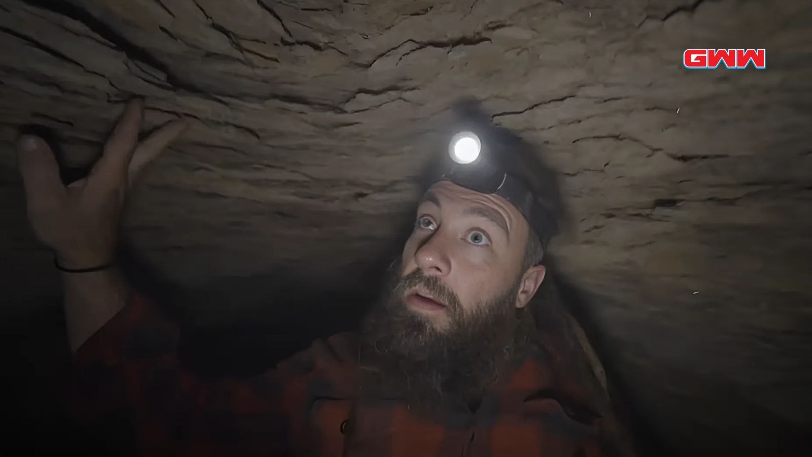 Charlie Snider cautiously exploring a tight cave passage with headlamp light