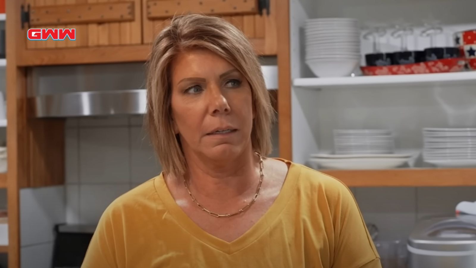 Meri Brownn with short hair wearing a yellow shirt in a kitchen.