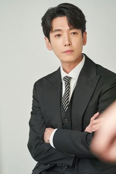 This contains a picture of Jung Kyung Ho in a suit and tie sitting down with his arms crossed looking at the camera