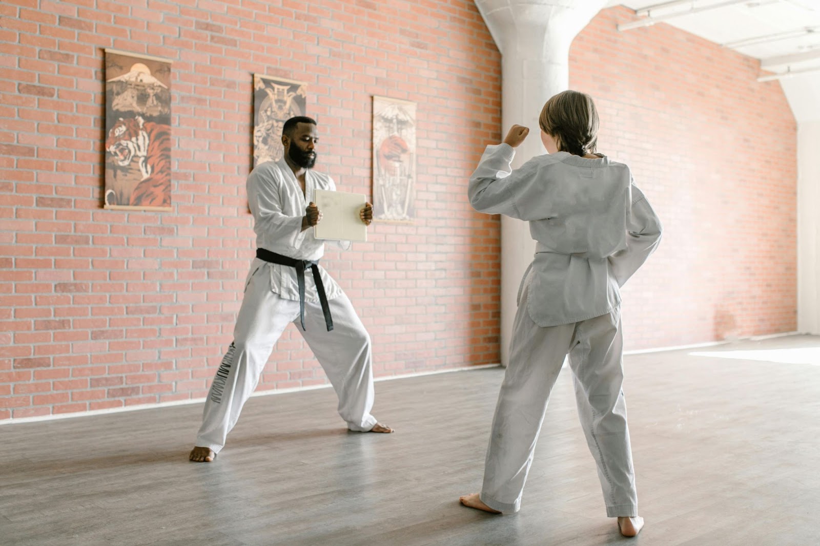 A martial arts instructor holds out a piece of paper in front of a young student, who is poised to punch it.