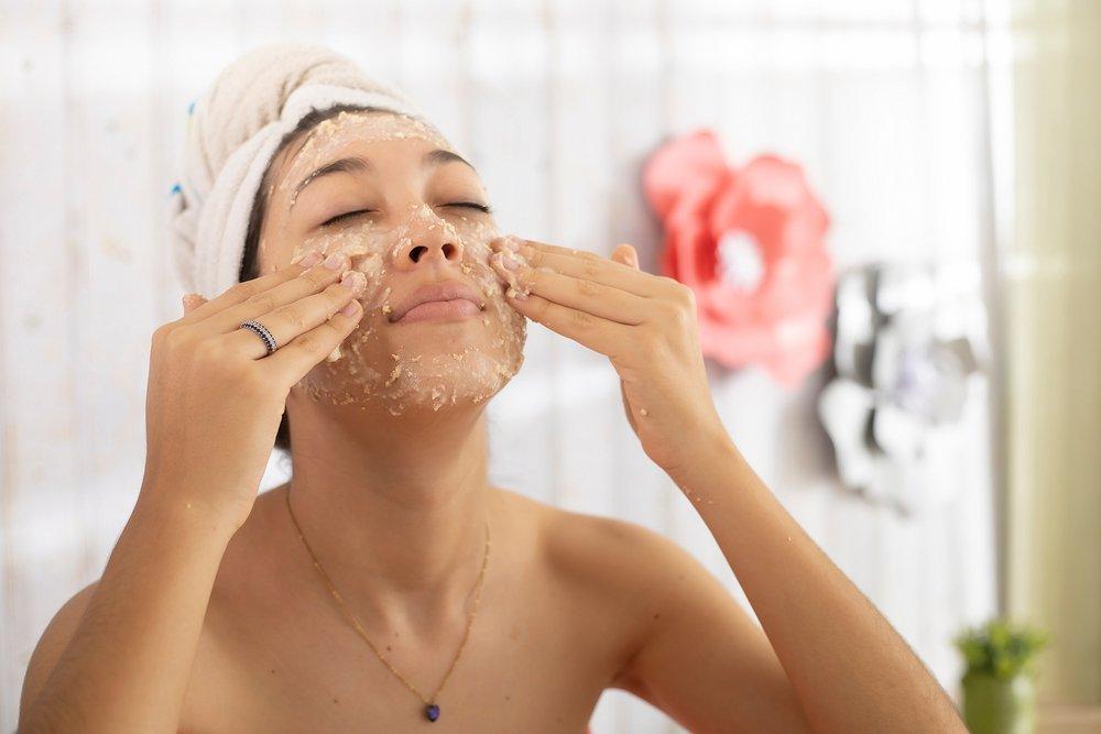 Woman applying oatmeal face mask at home.
