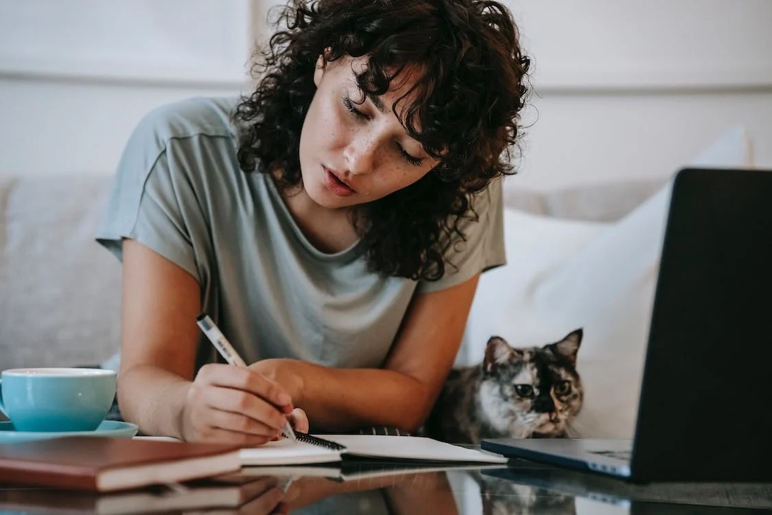 Focused young female student doing homework using netbook sitting near cute cat
