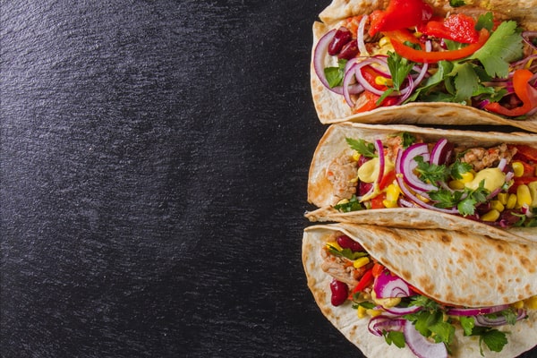 Three freshly made tacos filled with colorful vegetables, red onions, cilantro, and seasoned meat, served on soft tortillas