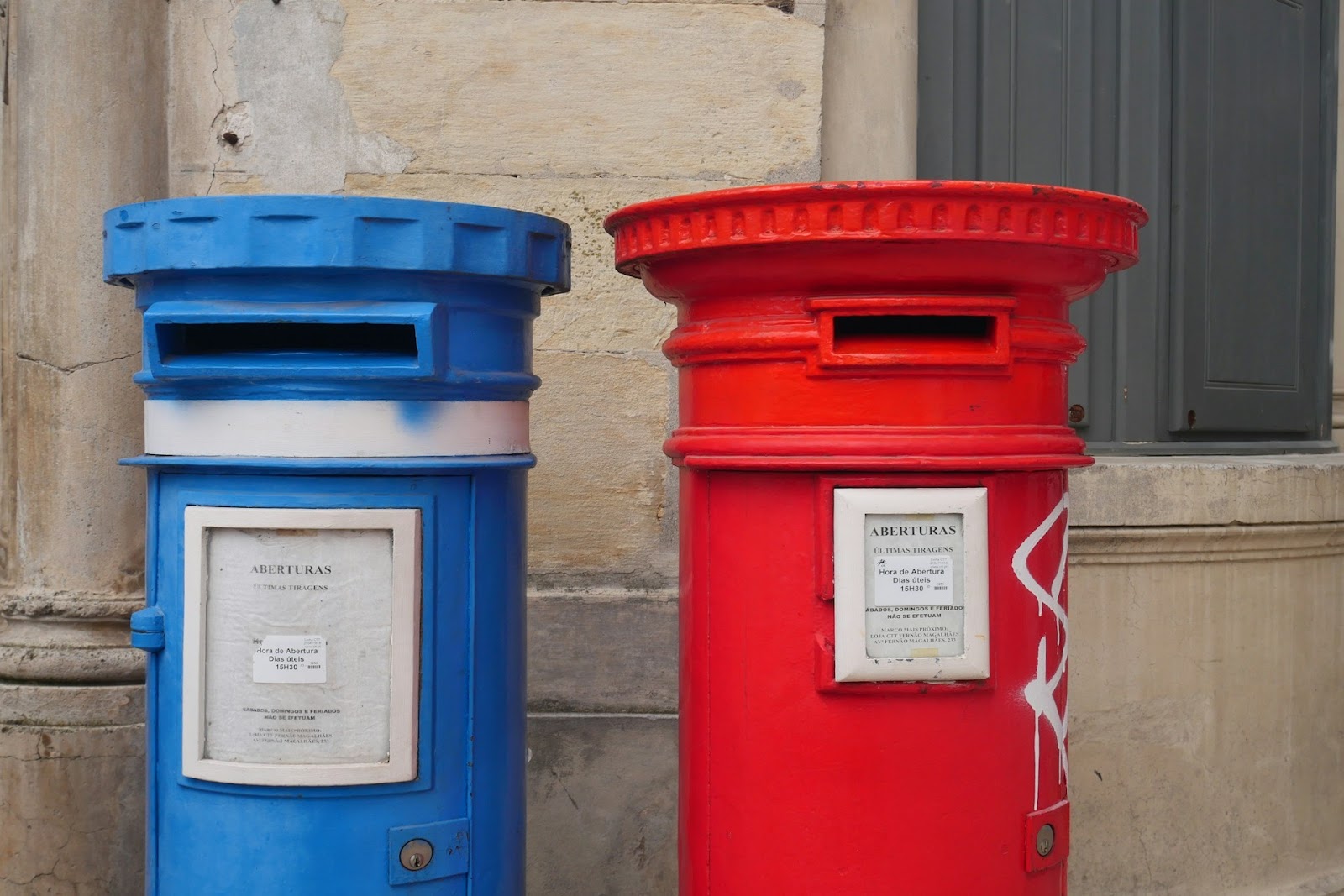 Red and blue mail boxes in front of a wall.