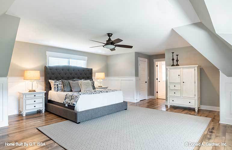 Bedroom with a tufted bed, white cabinets, and gray walls graced with white wainscoting.