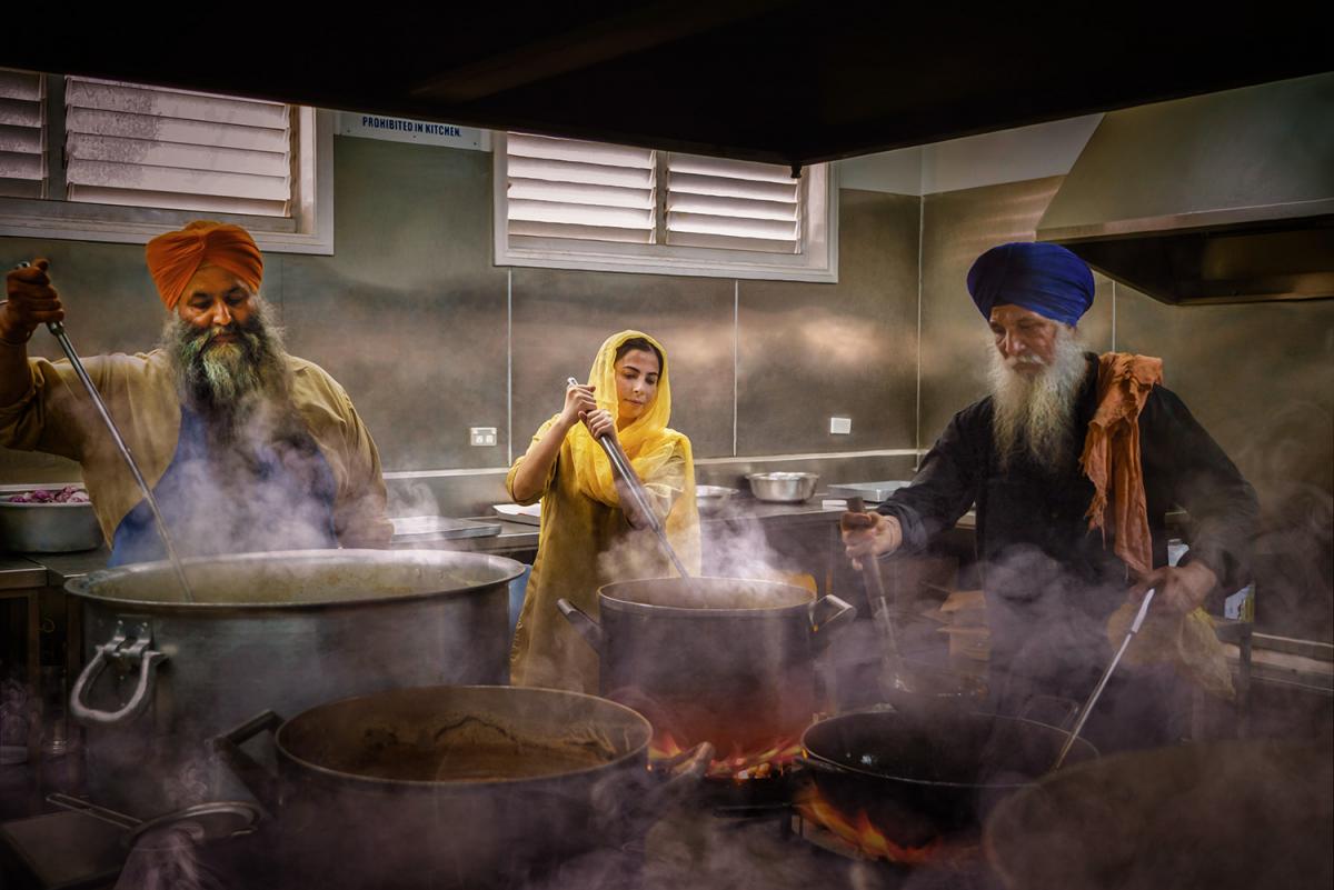 A photo of two men and a woman cooking meals in a langar.