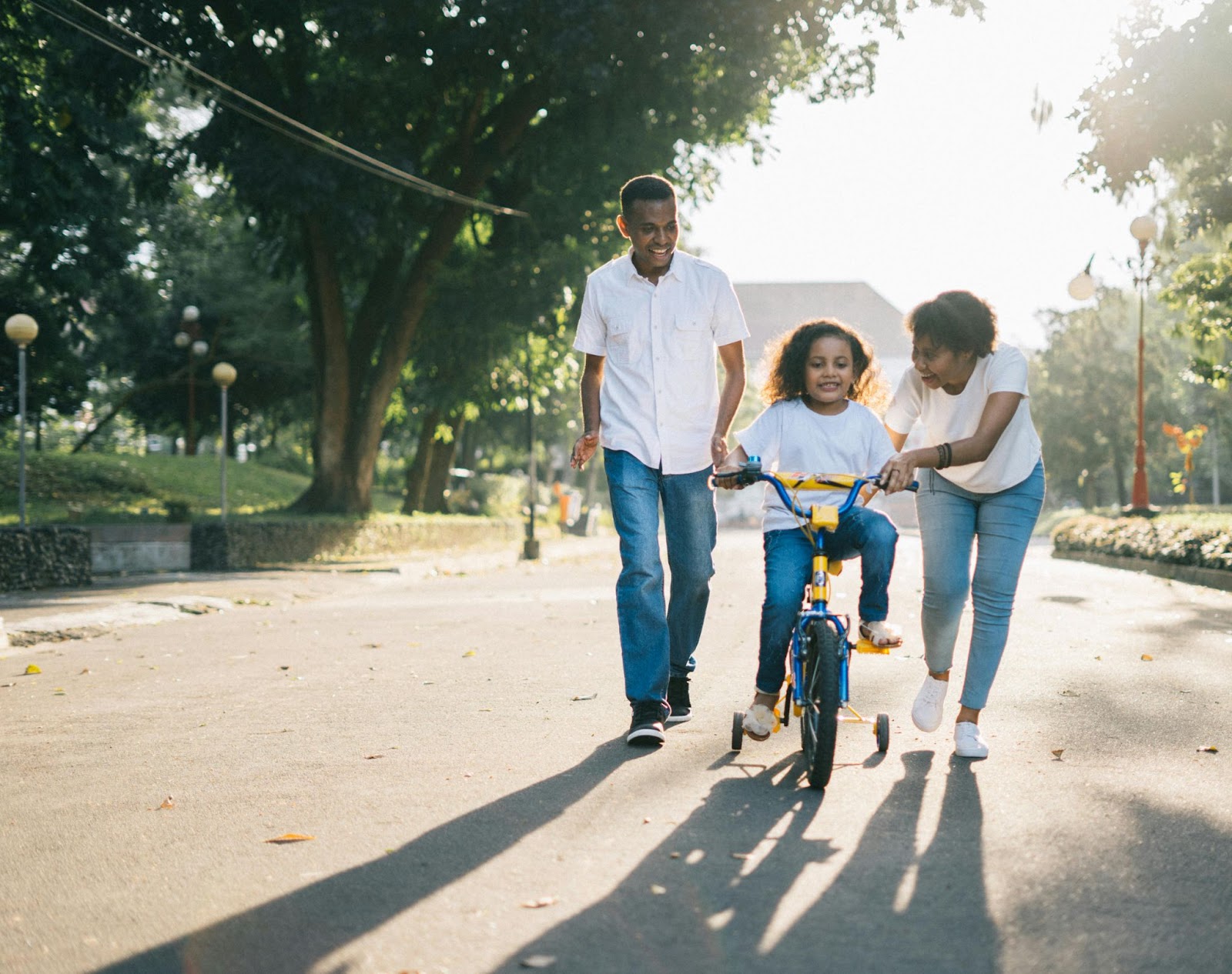 Two parents helping their young child ride a bike