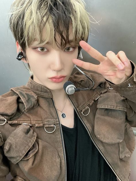 A picture of TheKingdom's Hwon wearing a brown jacket and a black inner vest with a handless mic on his ear 