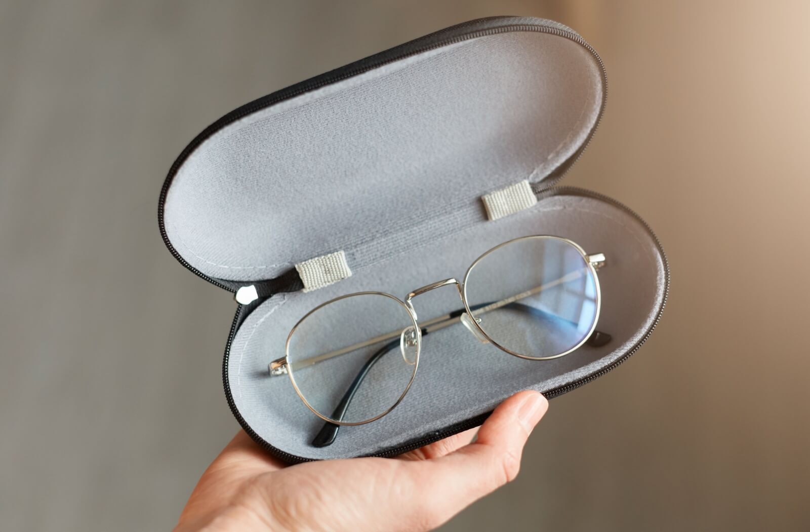 An individual holds up their protective eyeglasses case, showcasing their eyeglasses sitting inside