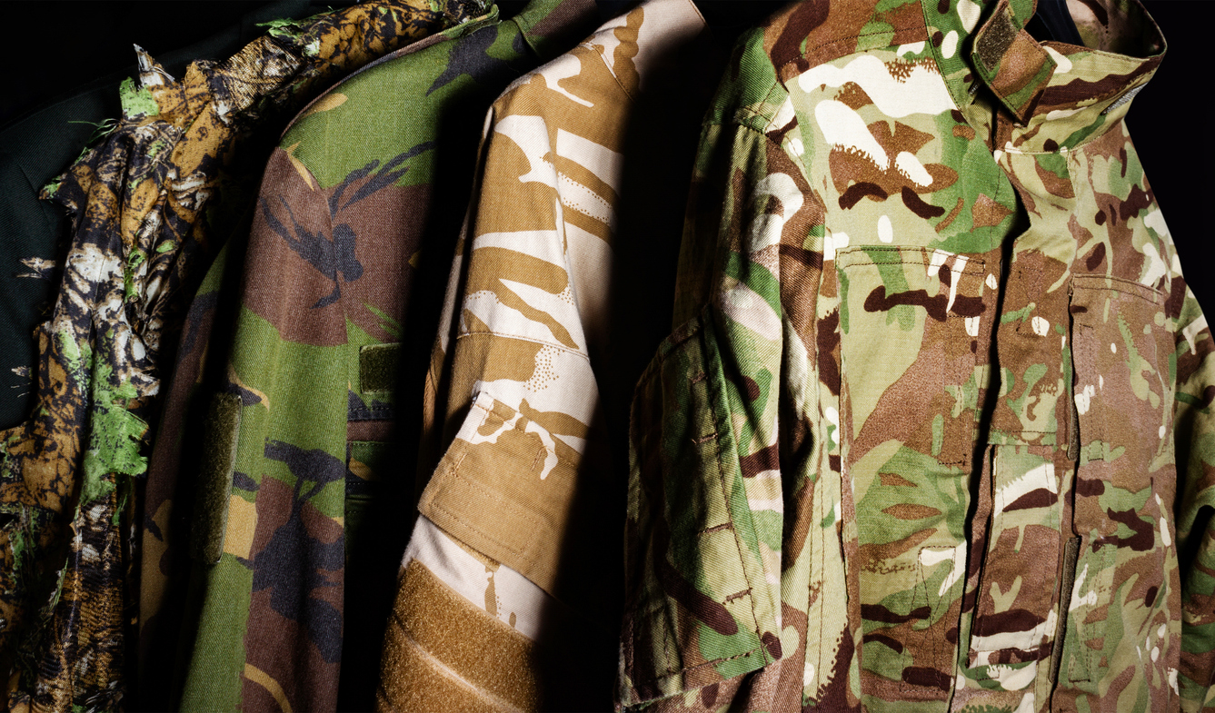 Camo jackets hanging up in a dark closet.