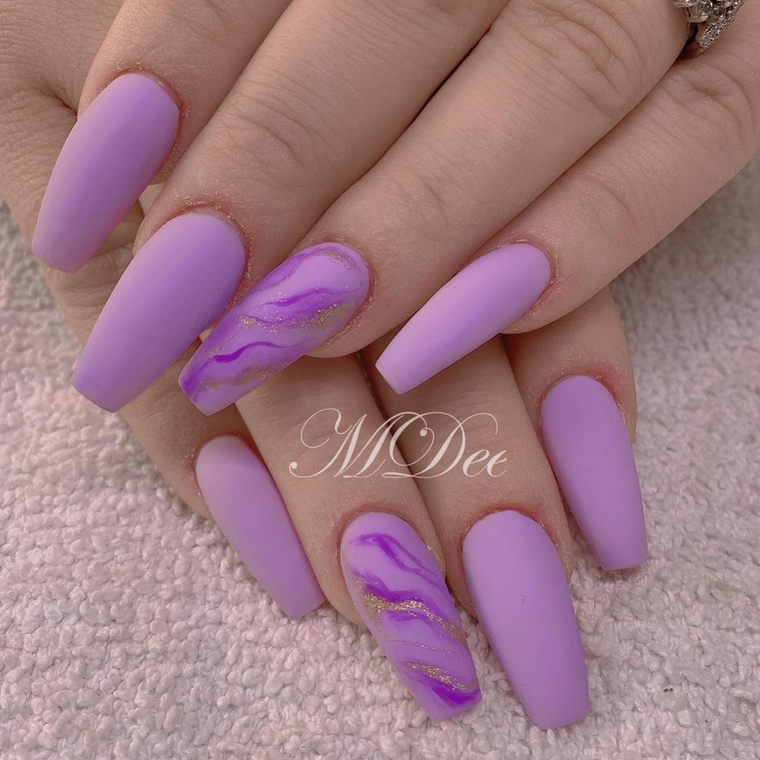 Close-up of hands with matte lavender nails. Ring fingers have wavy dark purple and gold glitter designs.