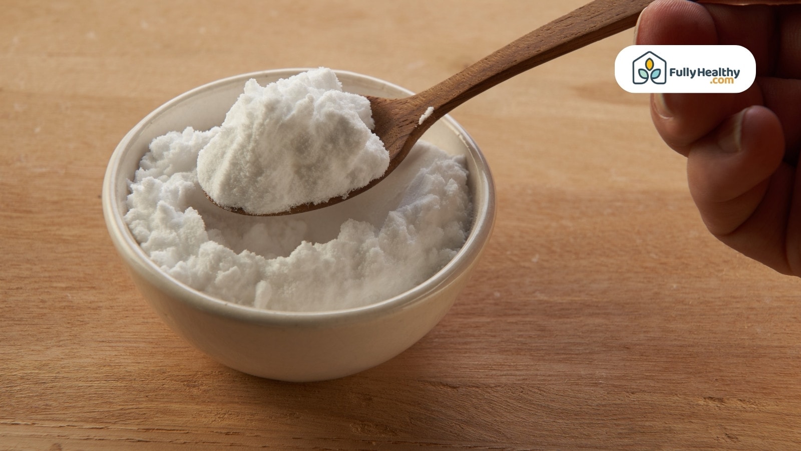 Wooden spoon scooping baking soda from small white ceramic bowl