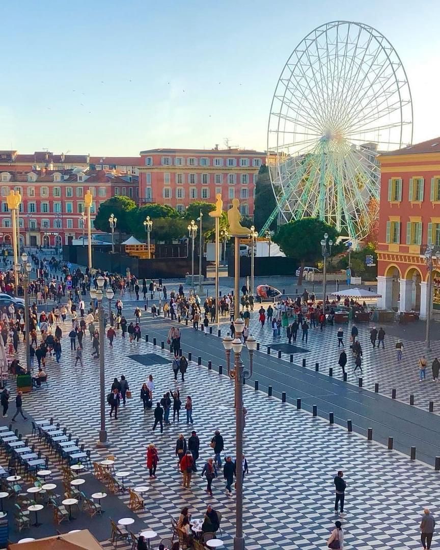 A large crowd of people in a square with a ferris wheel

Description automatically generated