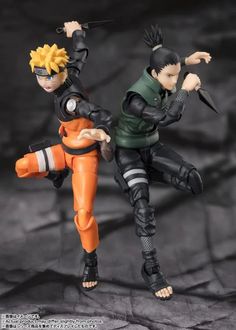 This may contain two action figures are posed together on a black and gray background, one is holding an orange object