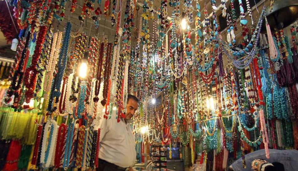 Colorful display of beads and jewelry in Bazaar Reza, Mashhad, Iran, showcasing a vibrant marketplace with hanging strands of beads and a vendor browsing through the collection.