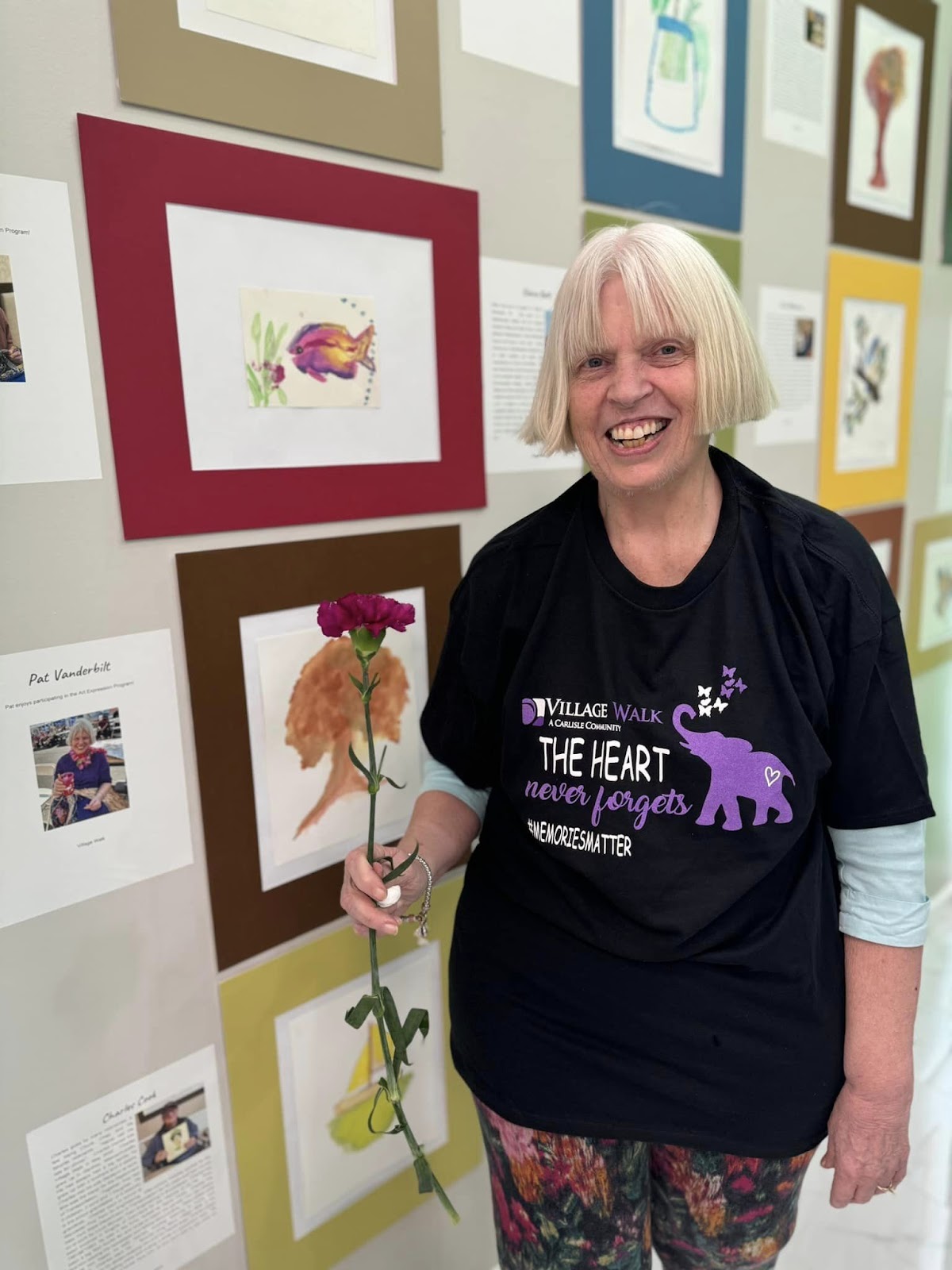 An assisted living resident smiling in front of artwork on a wall