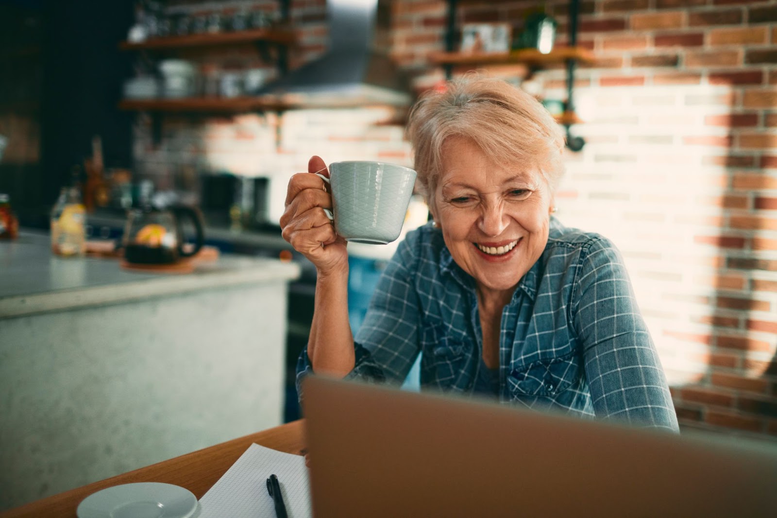 A happy senior sitting in her kitchen drinking coffee and planning ways to finance independent living.