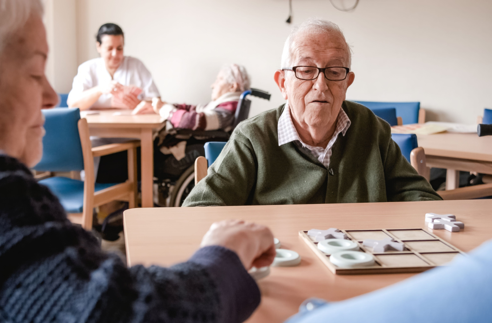 2 seniors play tic-tac-toe in the common area of their nursing home.