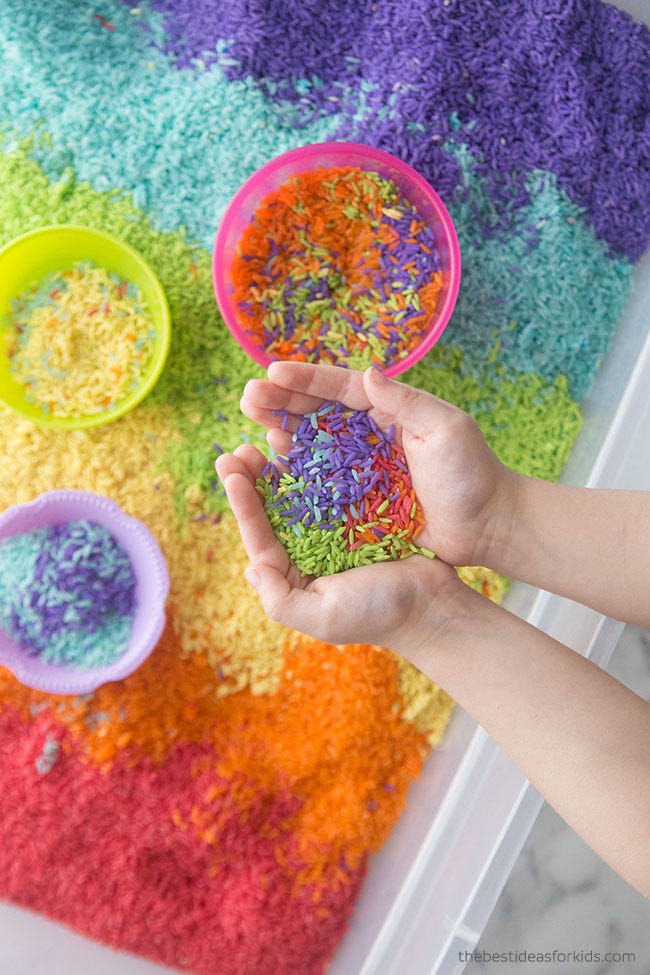 easter egg hunt ideas, hand holding colorful rice over a bin full of colorful rice