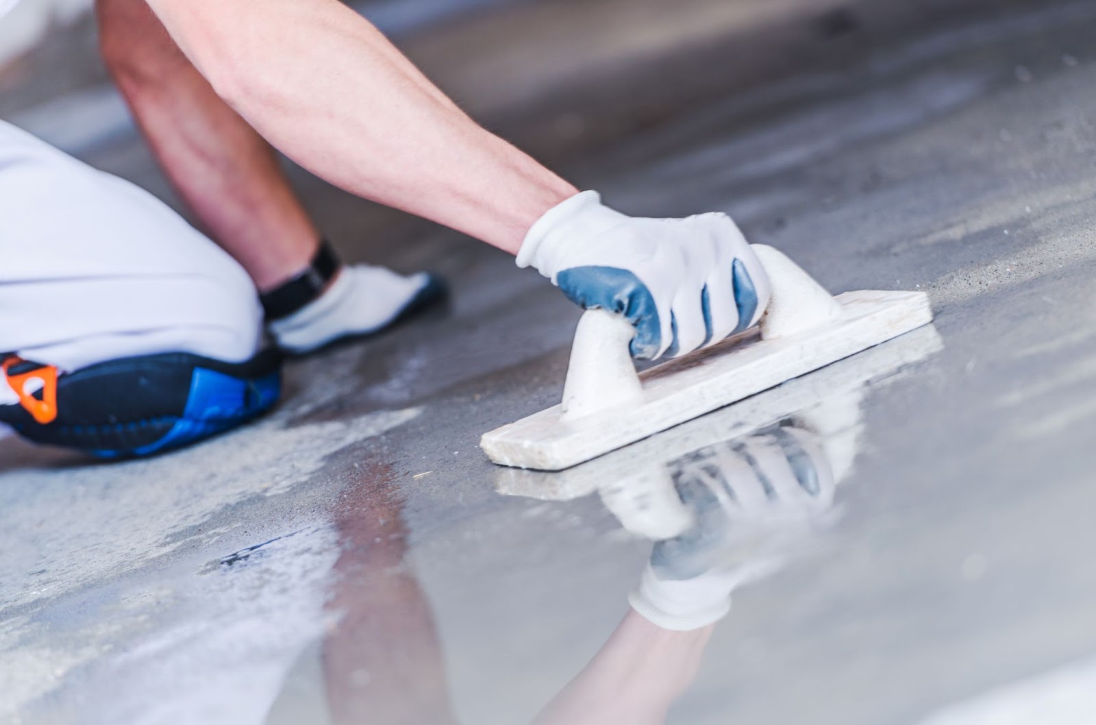 A cropped shot of a worker wearing safety gloves resurfacing concrete floors with a trowel.