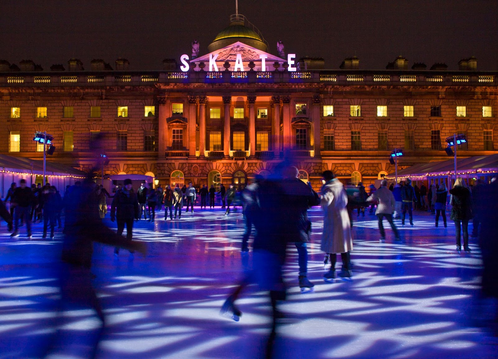 People ice skating at Somerset House in London, surrounded by festive lights and holiday decorations during the winter season